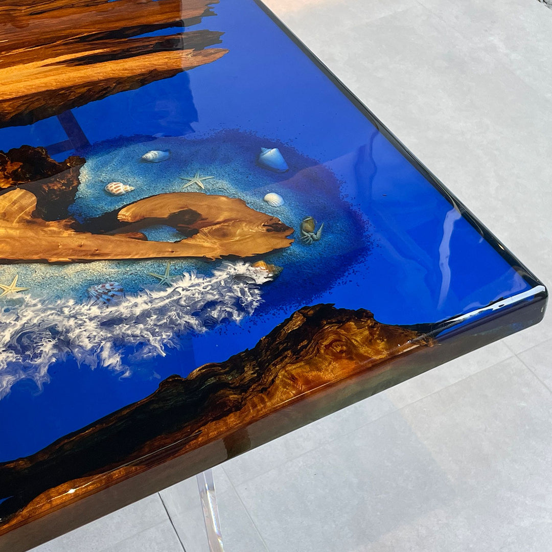 A close - up of a resin - topped wooden table with a detailed ocean scene, including shells and waves.