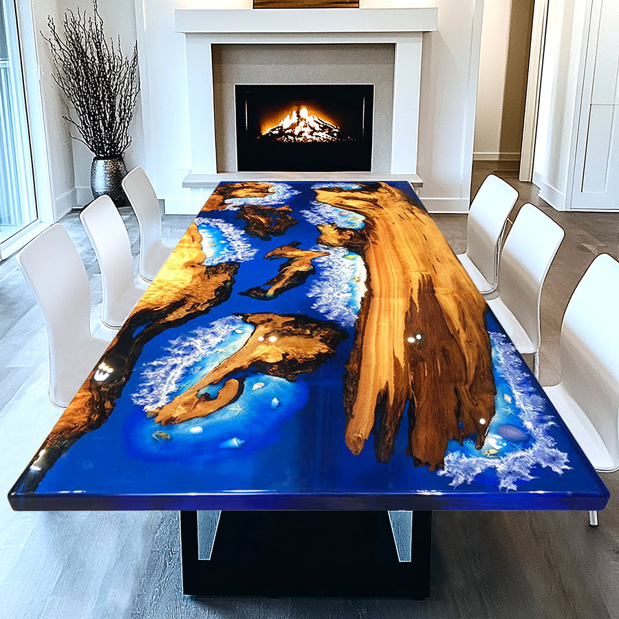A custom-made dining table with a blue epoxy resin top featuring wood embedded within, set in a room with a fireplace and white chairs.