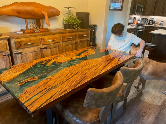 Customer photo of olive wood epoxy dining table with Mystic Lagoon resin base and clear top, styled in a modern home interior setting.
