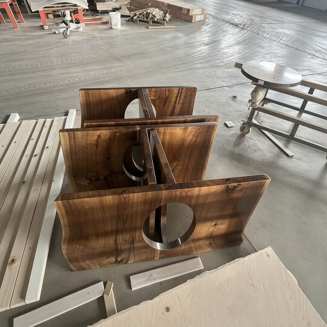 A set of rustic, wavy-edged wooden slats with circular cutouts, displayed on a concrete workshop floor alongside raw lumber and furniture pieces.