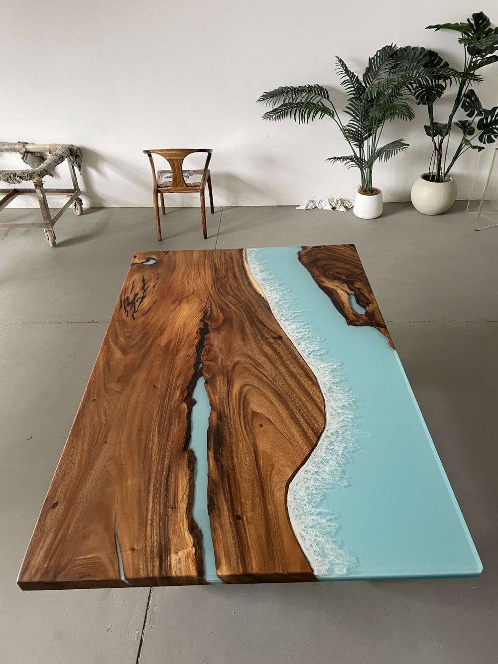 Wooden table with epoxy resin design in a room with plants and chairs.