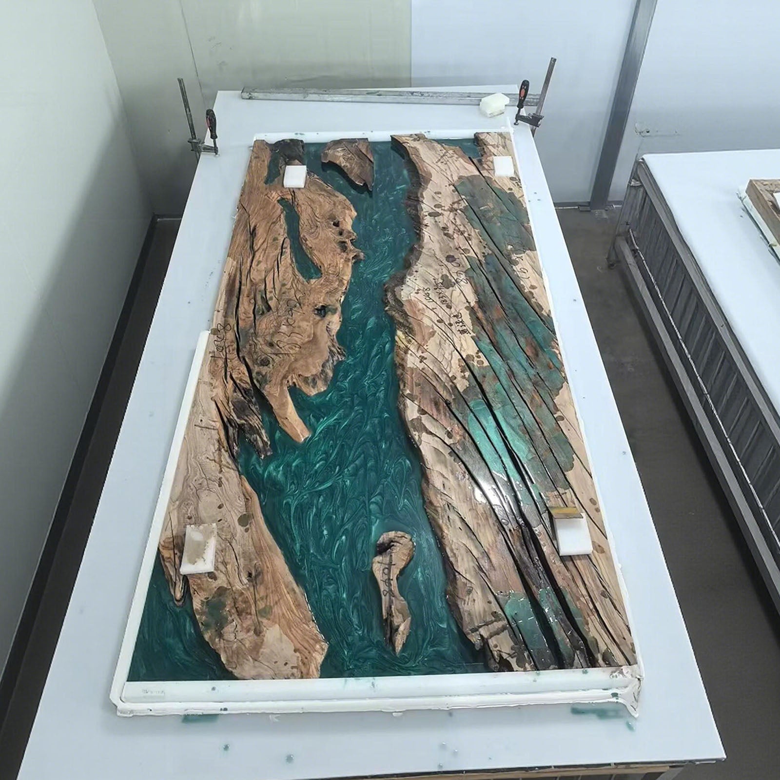 Side view of olive wood dining table with flowing Mystic Lagoon resin river, emphasizing straight edges and craftsmanship.