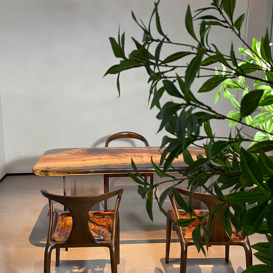 A resin - topped wooden dining table surrounded by matching chairs, set against a backdrop of greenery.
