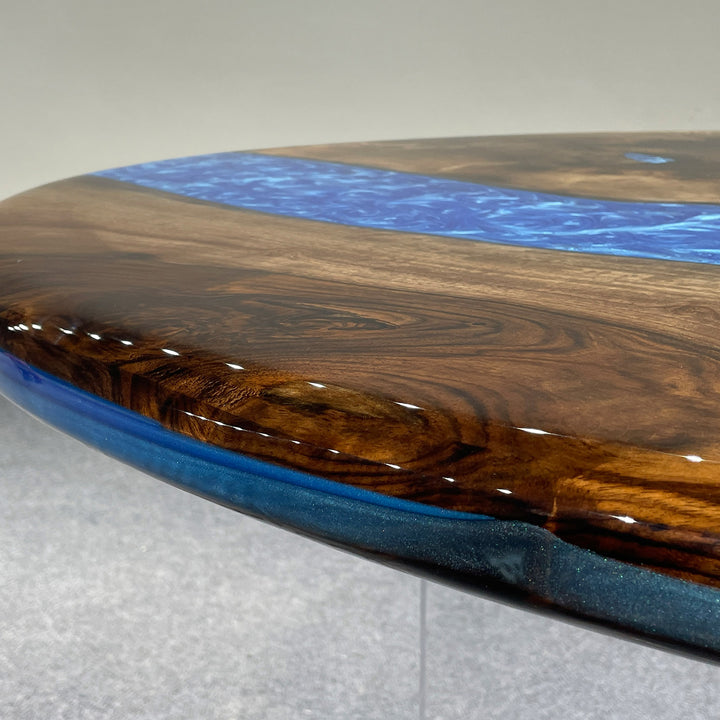 Swirling blue epoxy river flowing through solid black walnut oval table
