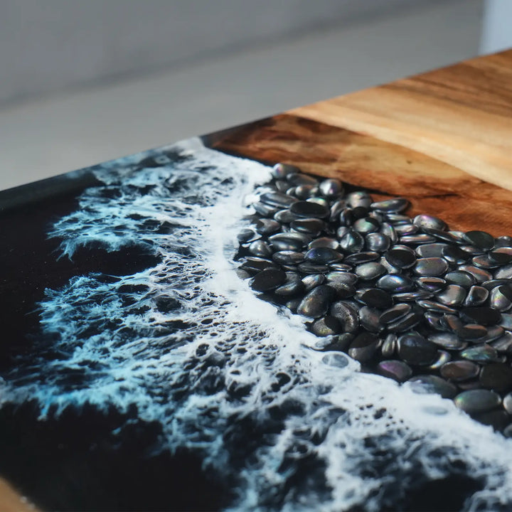 Close-up of white epoxy ocean waves and decorative black pebbles on a resin table