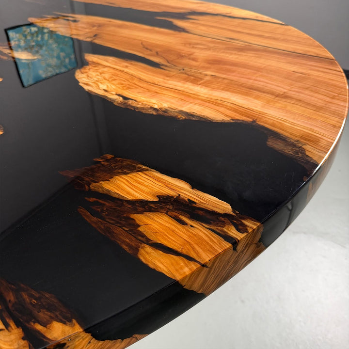 Close-up of the "Midnight Black" glossy epoxy resin river contrasted with the matte olive wood grain on a round dining table.