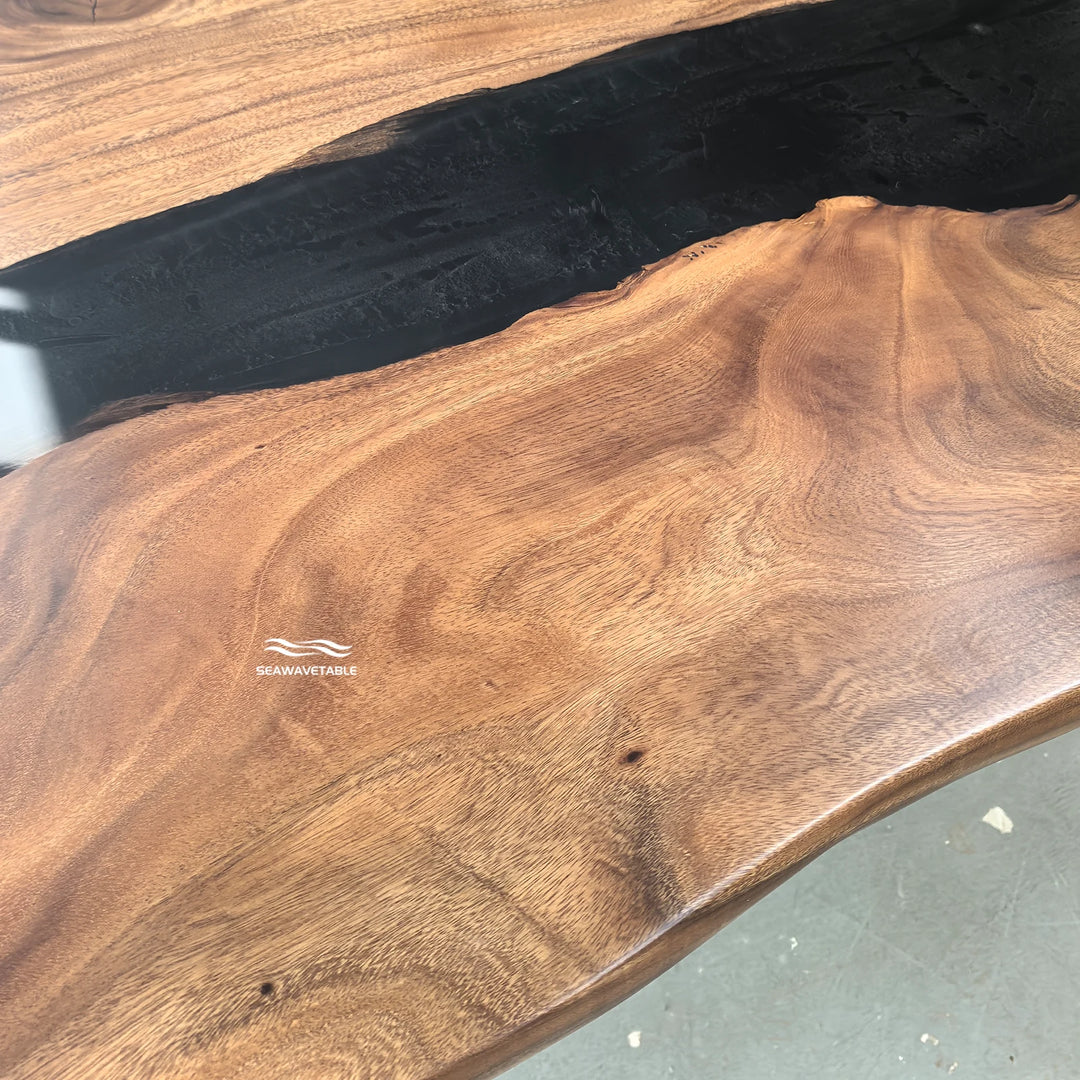 SeawaveTable-Close-up of a live-edge wooden tabletop with rich brown wood grain and a dark recessed channel, photographed indoors on a gray floor. A small 'HARAVAYABLE' watermark is visible on the wood surface.