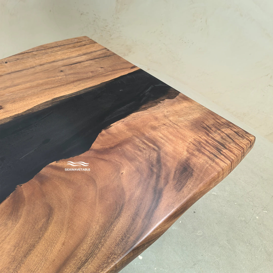 SeawaveTable-A close-up of a live-edge wooden table top with a rich brown wood grain and a prominent black resin inlay, photographed in an indoor setting.