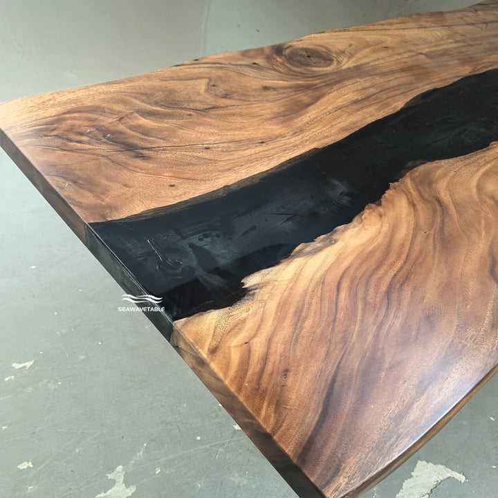 SeawaveTable-A close-up of a live-edge wooden table with rich brown wood grain and a glossy black resin river running through the center, photographed in a workshop setting.
