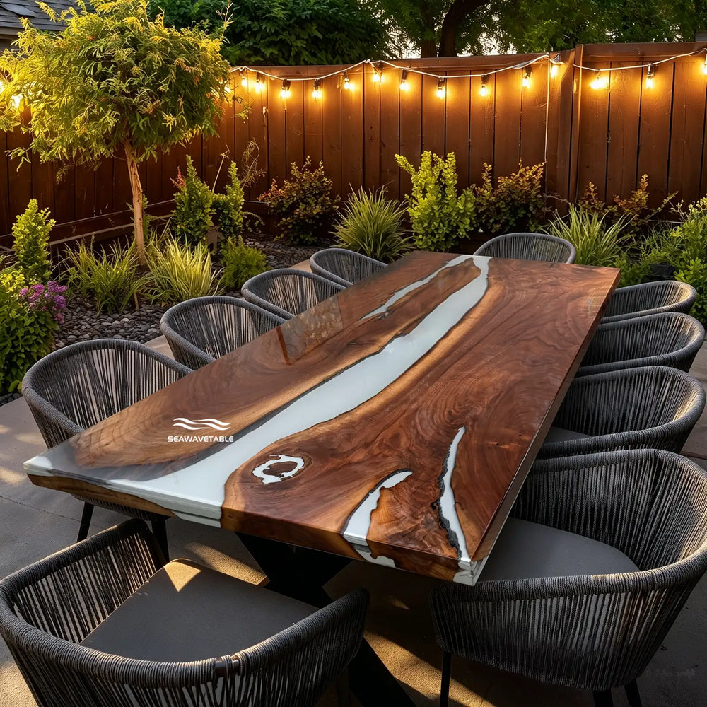 Custom solid wood dining table featuring a black walnut slab with flowing white resin inlay, placed in a bright outdoor dining setting with modern patio furniture and decorative planters - SeawaveTable