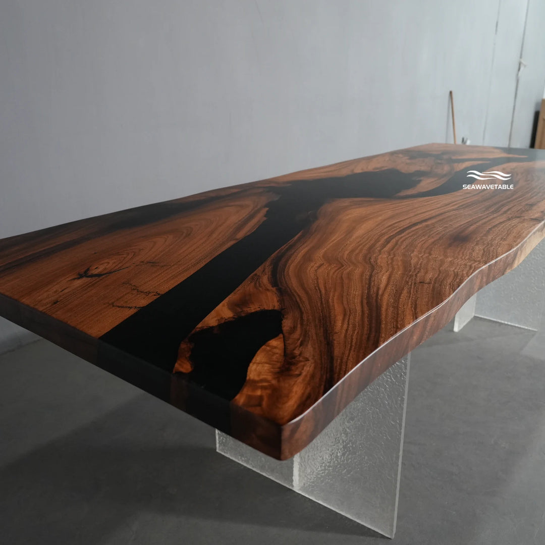 Seawavetable -A live-edge wooden table with a rich dark brown wood grain and a glossy black resin river running through the center, supported by clear acrylic legs.