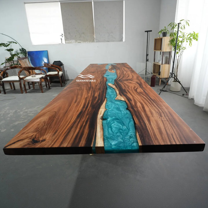 A long live-edge wooden table with a turquoise river design running down the center, photographed in a studio or showroom setting. The tabletop has visible wood grain and a white 'SERPENTINE' logo near one end.