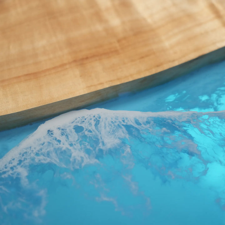Close-up detail of an epoxy table showing the vibrant blue ocean channel flowing through the natural poplar grain with smooth polished finish - SeawaveTable
