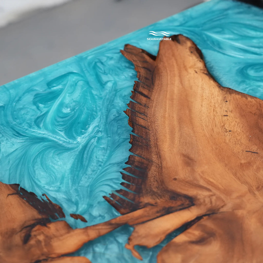 A close-up of a sculptural resin tabletop featuring a bright turquoise blue marbled wave-like pattern and a large natural wood slice with dark brown grain and irregular edges.