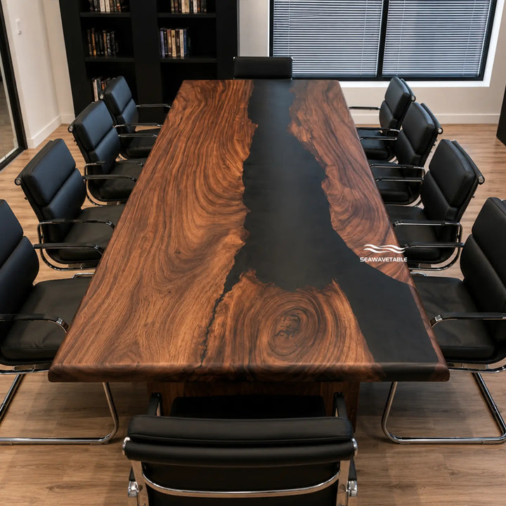 A large rectangular conference table with a rich brown wood grain and a glossy black resin center channel, surrounded by black office chairs in a modern office setting. A watermark logo for 'SHAWKISTABLE' is visible on the right side of the table.