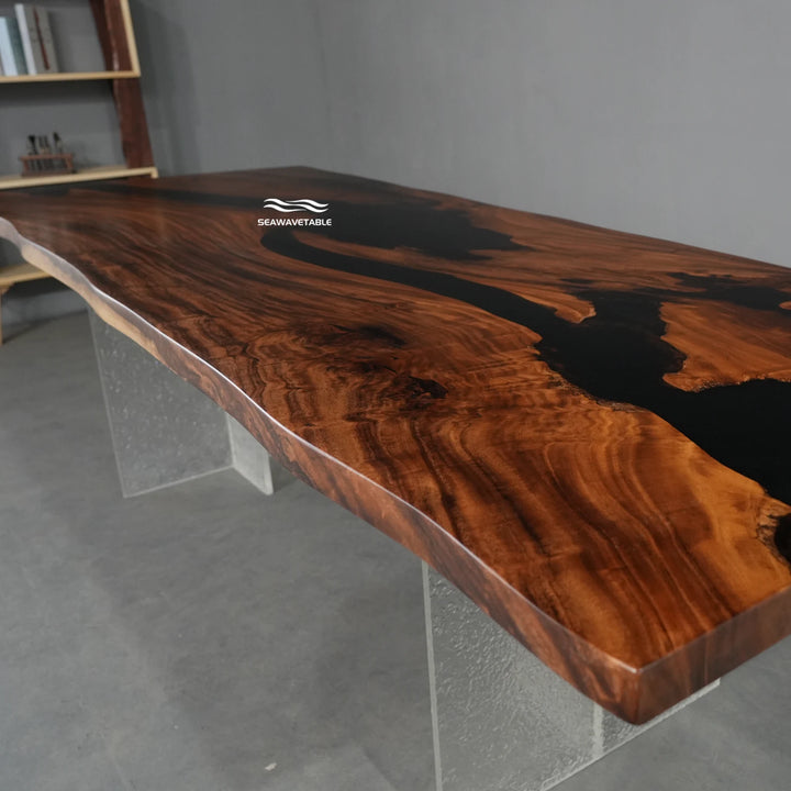  Seawavetable-A live-edge wooden desk with a rich, polished brown wood grain and a black resin inlay, supported by clear acrylic legs in a modern studio setting.
