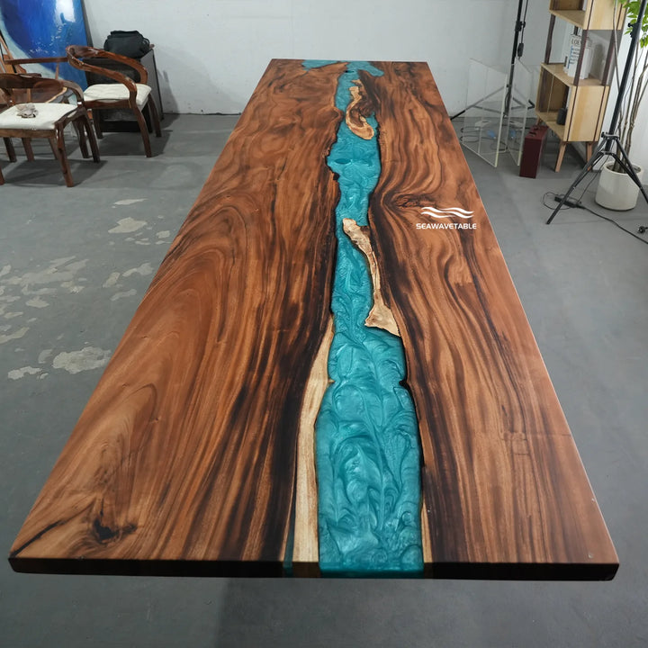 A large live-edge wooden table with a prominent turquoise river design running down the center, photographed in a warehouse or showroom setting.