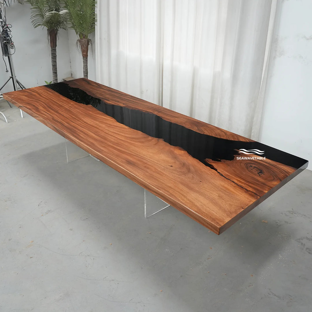 A long live-edge wooden table with a glossy black river design running down the center, supported by slim metal legs in a studio setting with white curtains and a concrete floor.