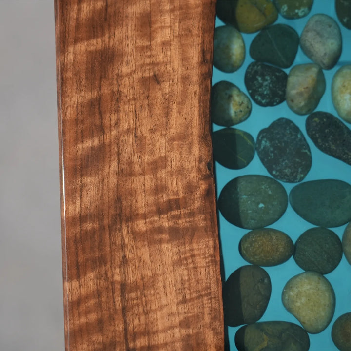 Seawavetable-closeup view of transparent blue epoxy resin with small stones in black walnut console table