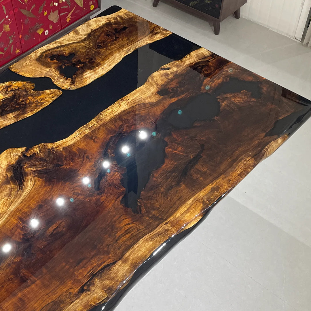 Seawavetable-A large live-edge wooden table with a glossy dark resin finish, photographed from an elevated angle in an indoor showroom. The wood grain is prominent in warm brown and amber tones, with dark black resin channels running through it.