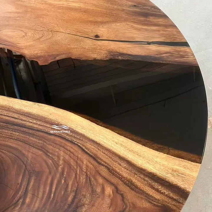 Seawavetable-A close-up of a live-edge wooden tabletop or tray showing rich natural wood grain, with a dark resin inlay running through the center and a small white logo watermark near the bottom.