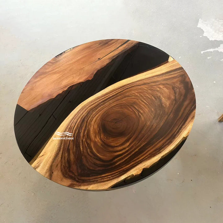 Seawavetable-A round live-edge wooden table top with a rich wood grain pattern, featuring a dark brown center, swirling grain, and contrasting light and dark wood sections, photographed from a top-down angle on a gray concrete floor.
