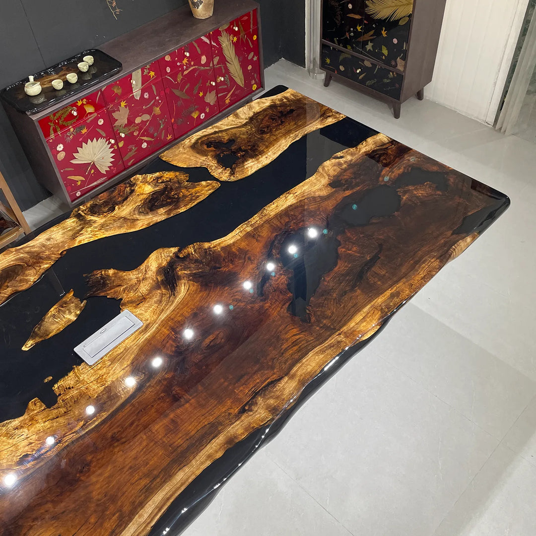 Seawavetable-A large live-edge wooden table with a glossy black resin top featuring natural wood grain patterns, shown in a modern room setting.