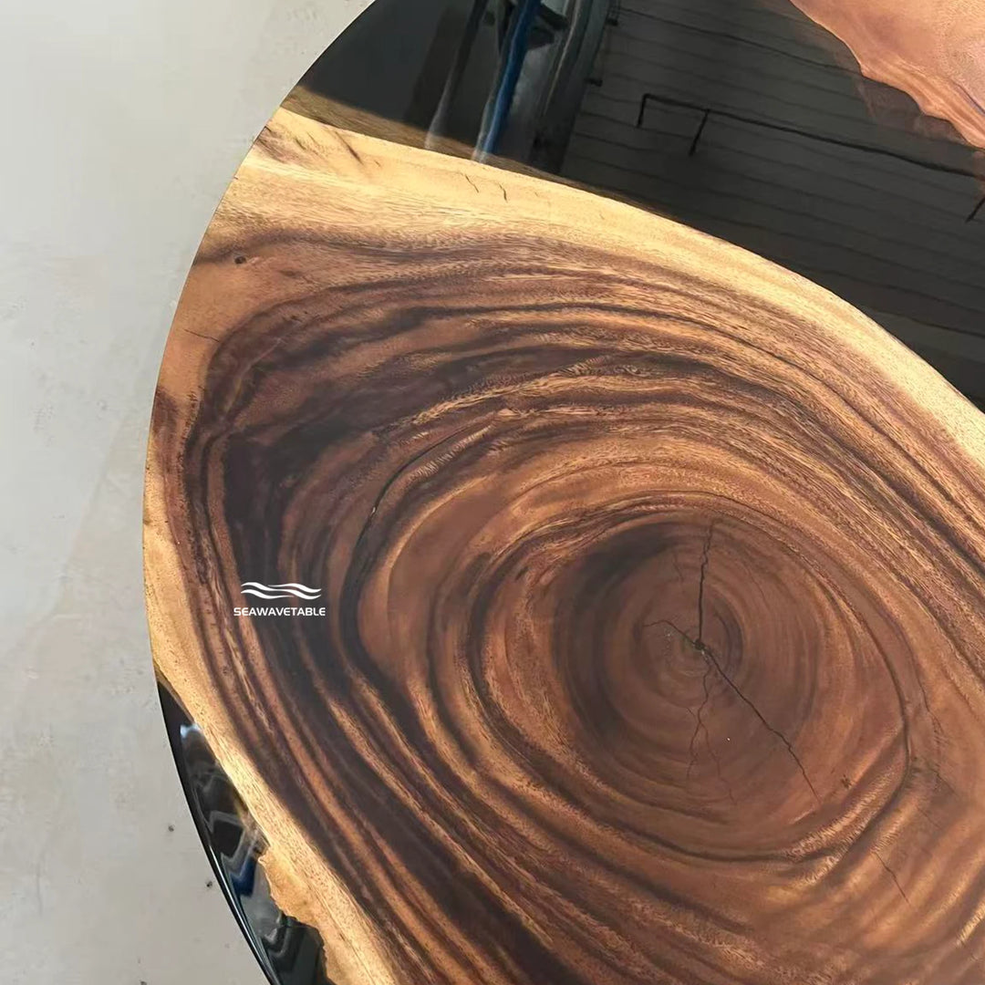 Seawavetable-A close-up of a live-edge wooden tabletop showing a rich natural wood grain pattern with concentric rings and a prominent center knot. The brand name 'SEAMAVETABLE' is printed on the wood surface.