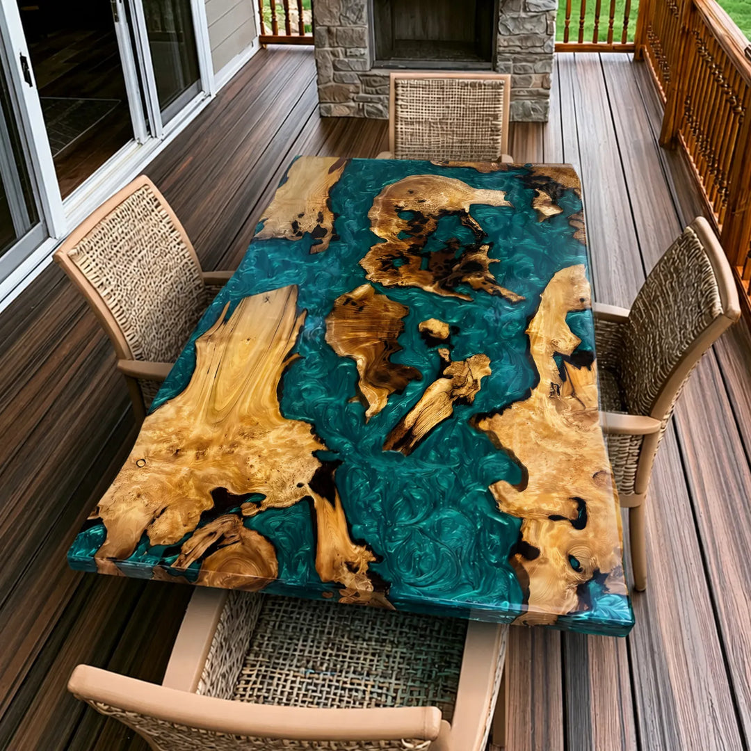 Seawavetable -A long live-edge wooden dining table with a glossy black resin flow and natural wood grain, surrounded by upholstered dining chairs in a modern stone-walled interior with large windows overlooking water.