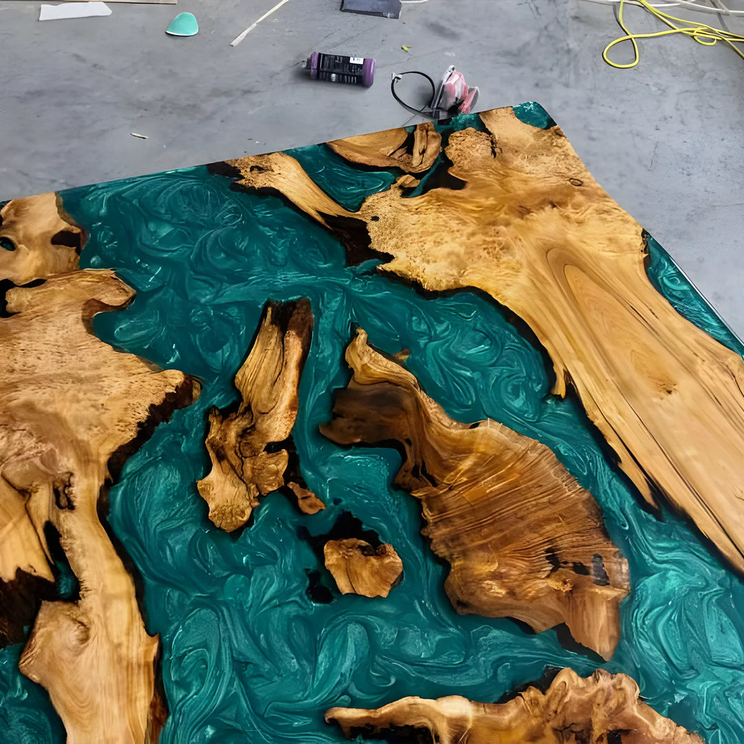 Seawavetable-A large live-edge wooden tabletop with swirling teal resin in the center, photographed from above on a concrete floor. The wood edges are prominent and natural, with no people or animals present.