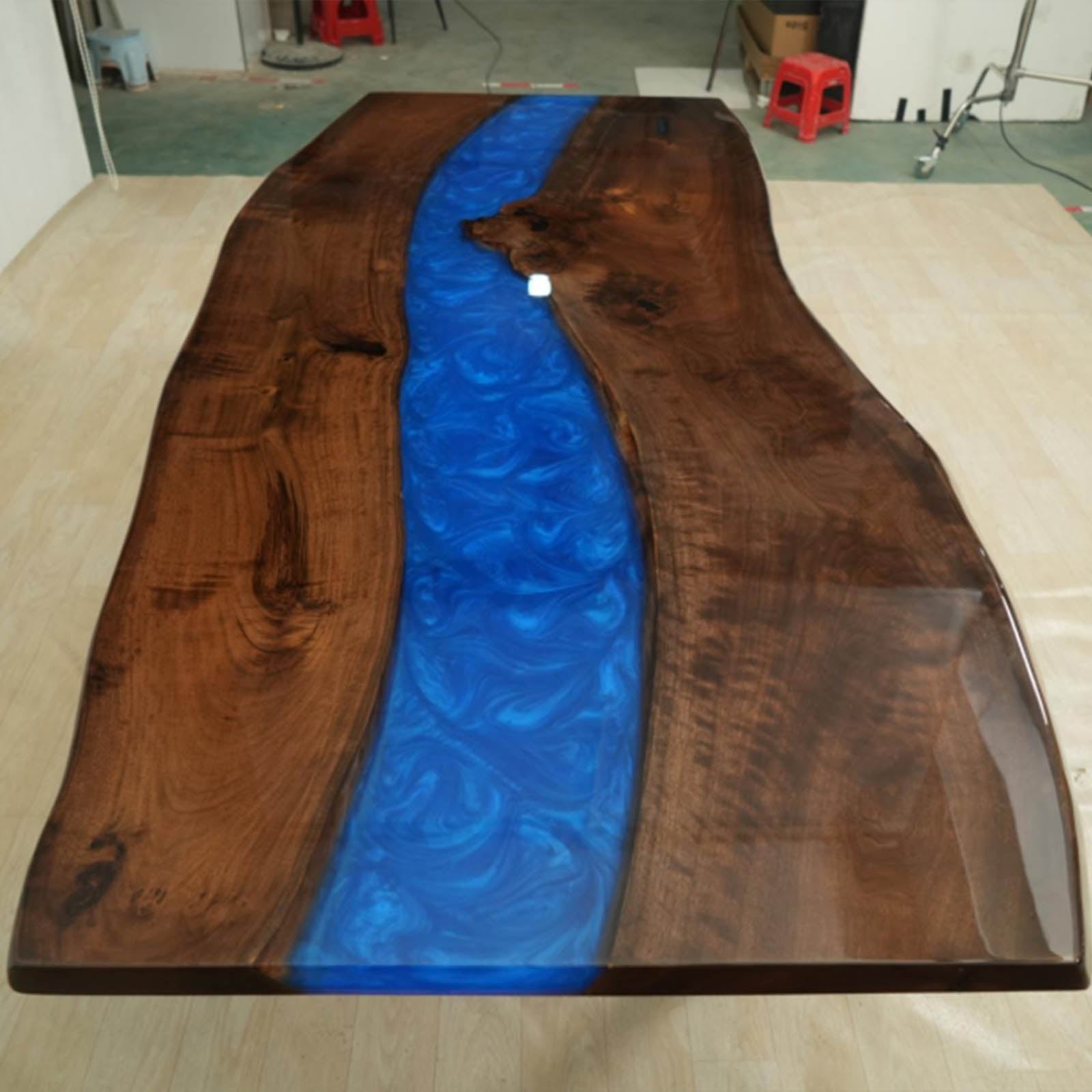 Close-up of swirling ocean blue resin river and LED lighting embedded in a live edge black walnut table surface.