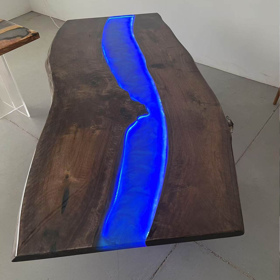 Black walnut live edge river table with swirling ocean blue resin and LED lighting glowing at night, creating a modern and dramatic atmosphere.