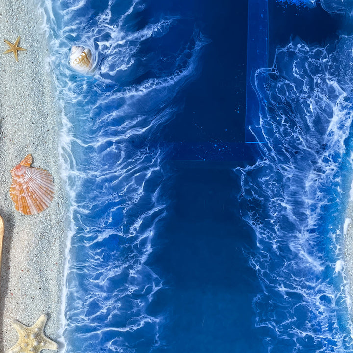 Close-up of a beach with blue water, sand, and shells.