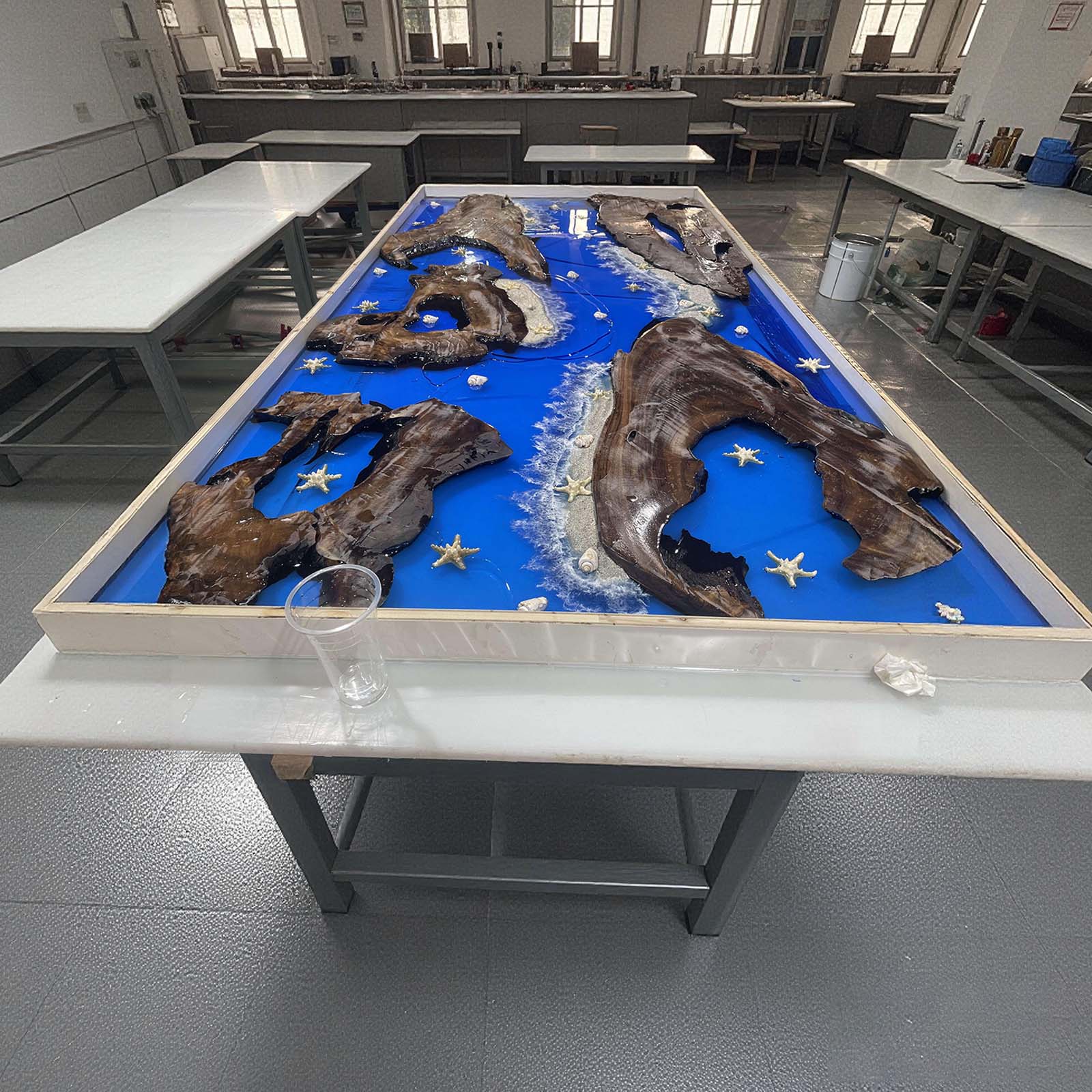 One-of-a-kind handcrafted golden camphor wood river table with transparent blue resin and beach elements, custom made in Pennsylvania near me.