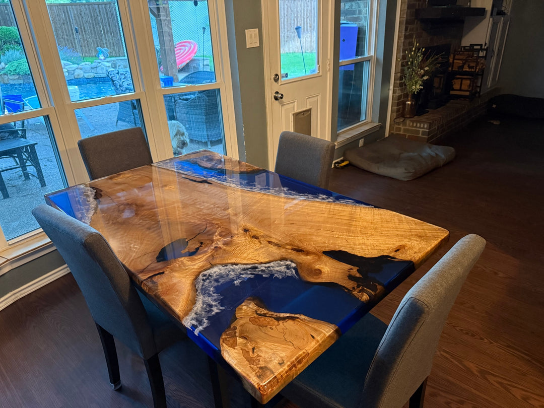 Golden camphor wood dining table with clear blue ocean wave epoxy design, straight edges, and a high-gloss surface finish.