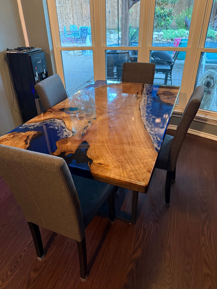 Close-up of clear blue epoxy resin with white ocean wave patterns flowing across golden camphor wood, finished in full gloss for a reflective surface.