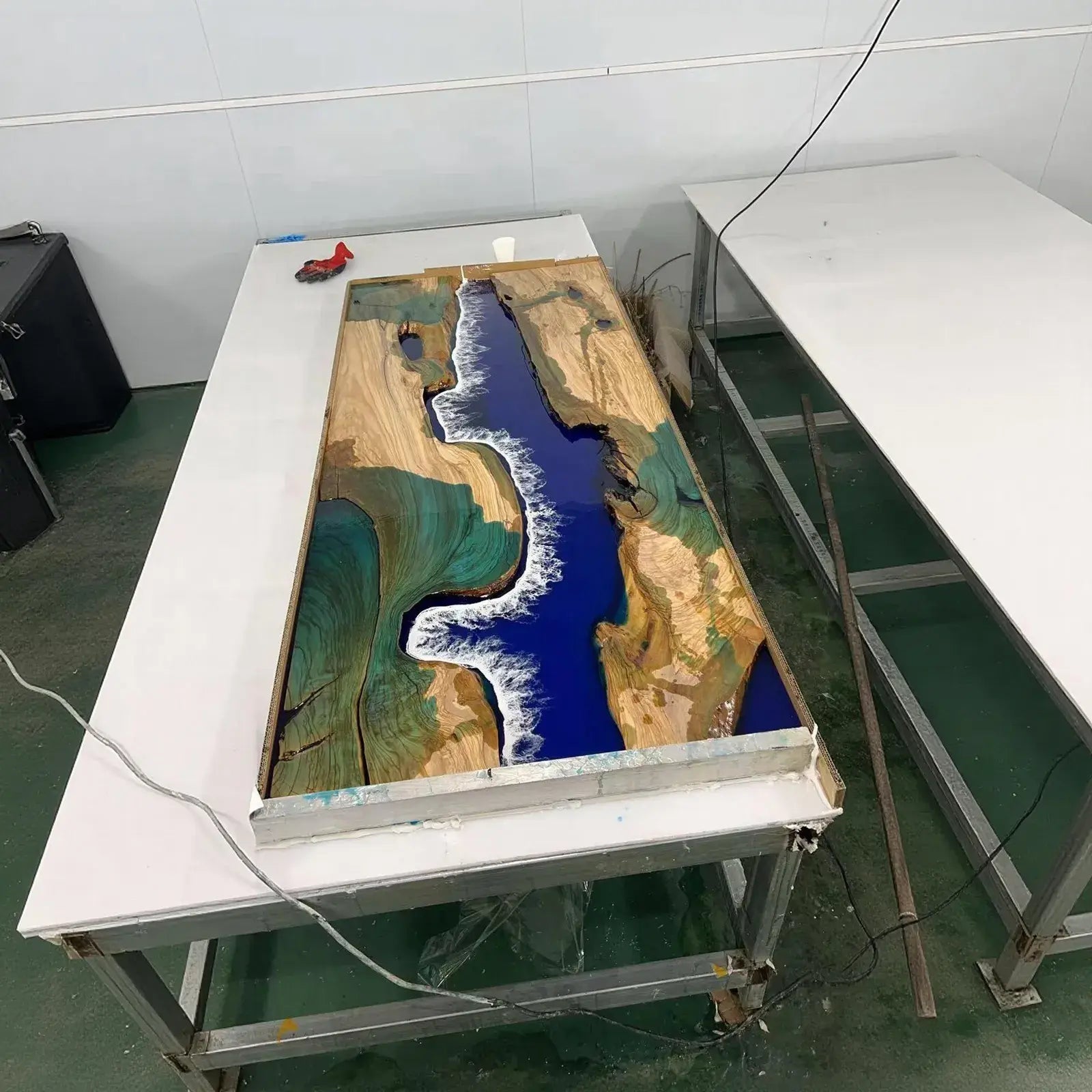 SeawaveTable pouring ocean blue epoxy resin into olive wood slab table mold